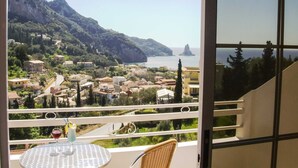 Varanda com mesa e cadeiras, vista para uma cidade costeira com edifícios e uma montanha.