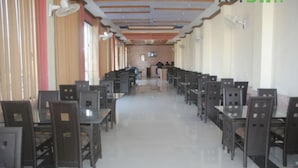A long corridor with rows of tables and chairs, a reception desk at the end, and ceiling fans. - Hotel River side and Restaurant (Swat)