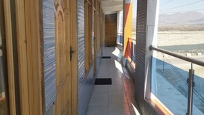 A corridor with wooden doors and a tiled floor, leading to a balcony with a view of a landscape. - Hotel River side and Restaurant (Swat)