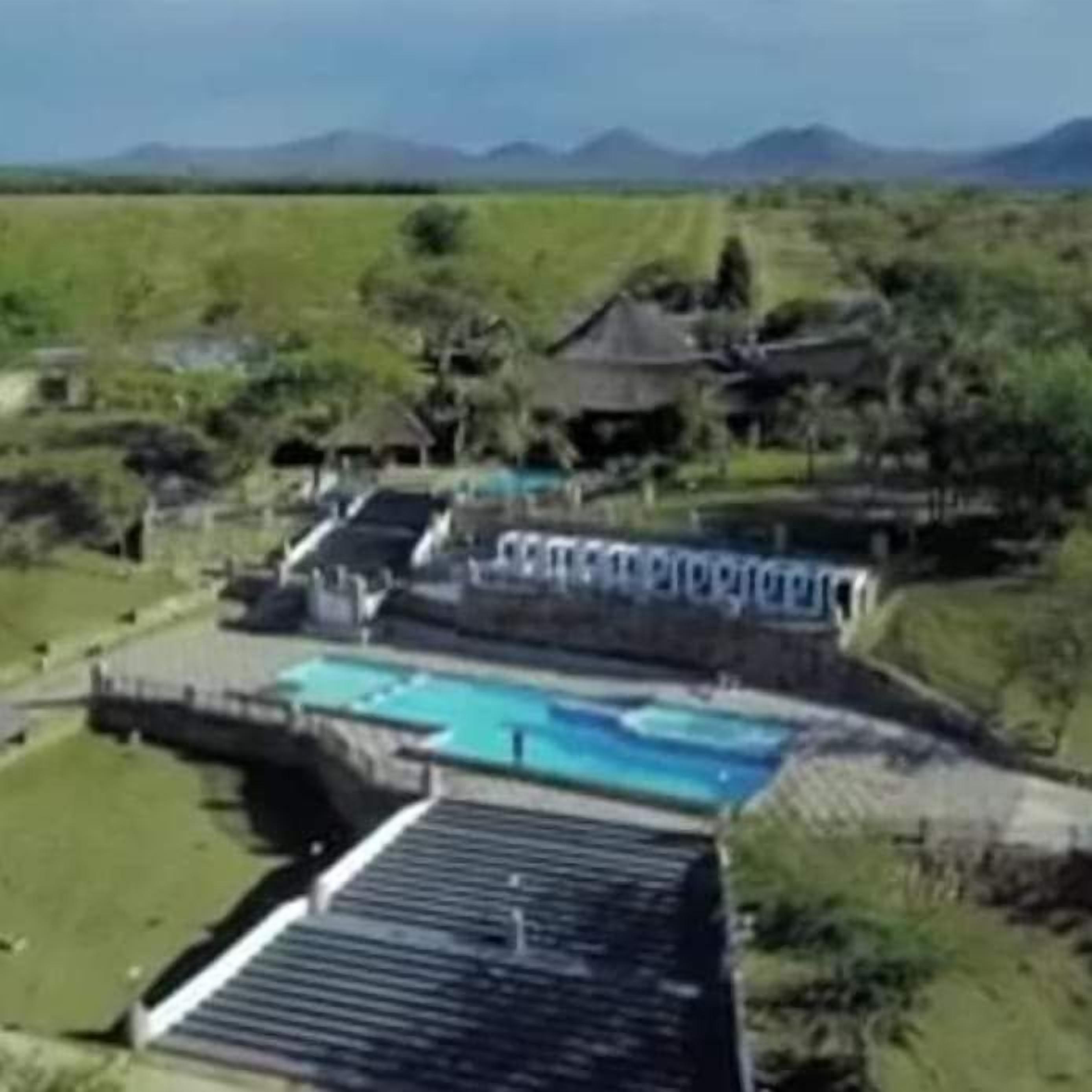 A resort with a swimming pool, a covered area, and a view of the surrounding landscape.