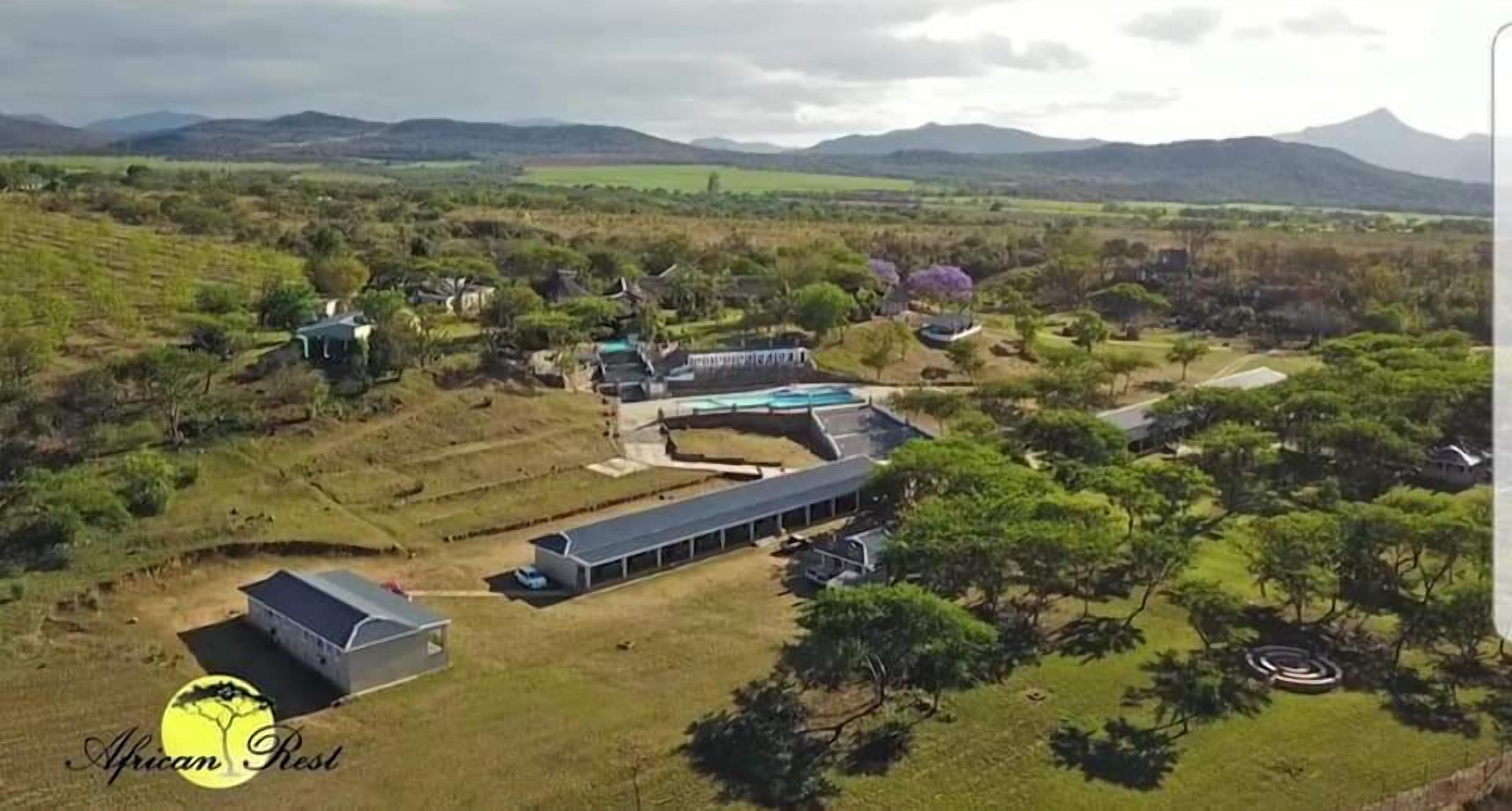 An aerial view of a property with multiple buildings, including a long structure with a flat roof, possibly a restaurant or communal area, and several smaller buildings with distinct roofs.