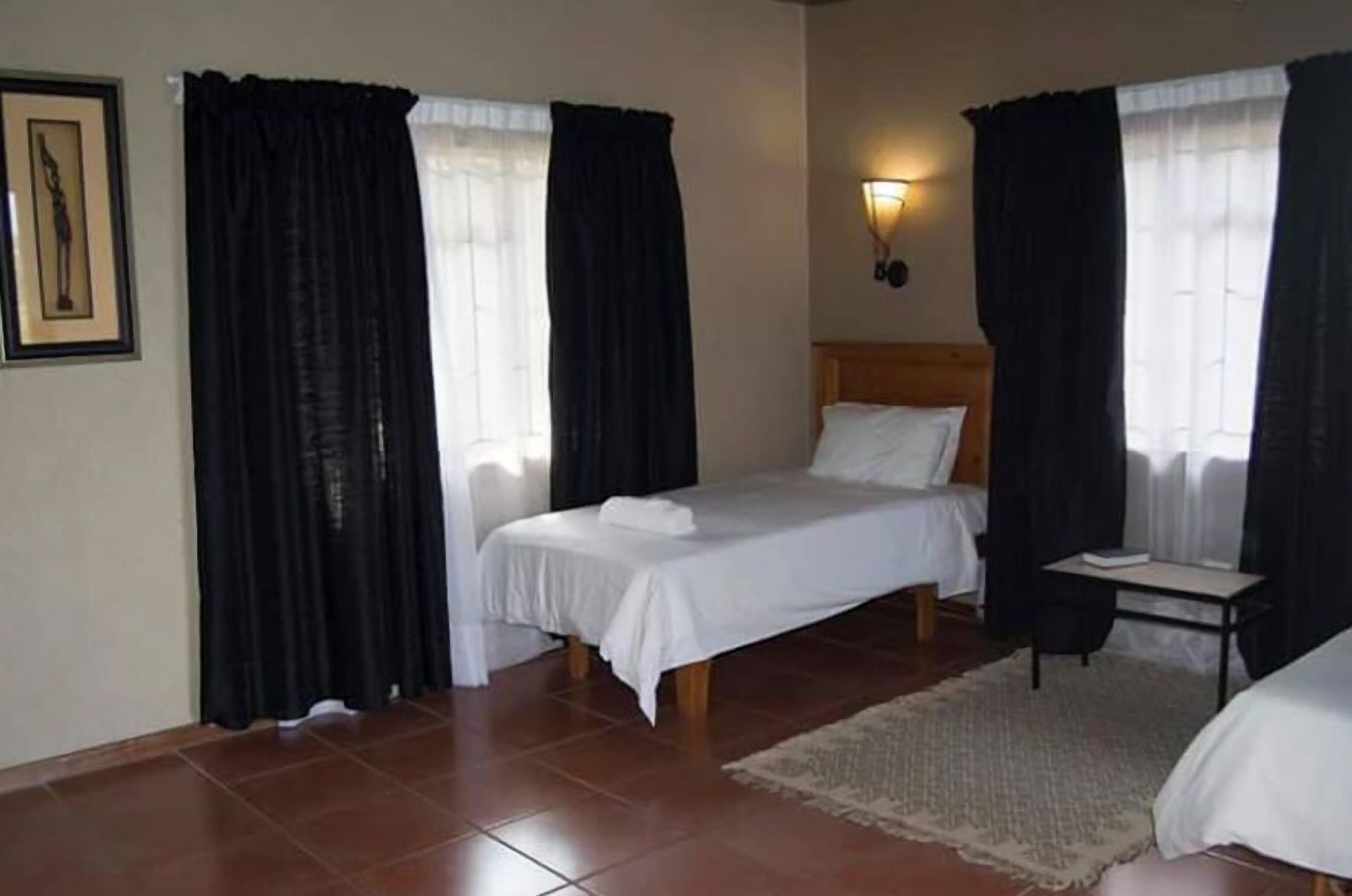 Habitación de hotel con una cama individual, una mesita de noche, una silla y un aplique de pared.
