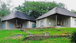 Two thatched-roof cottages with stone walls and a grassy slope. - African Rest Lodge (Barberton)