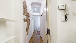 Un couloir étroit doté d’un plancher en bois, de murs blancs et d’un mur en briques apparentes. Une porte se trouve sur la droite, avec un téléphone et un interrupteur.