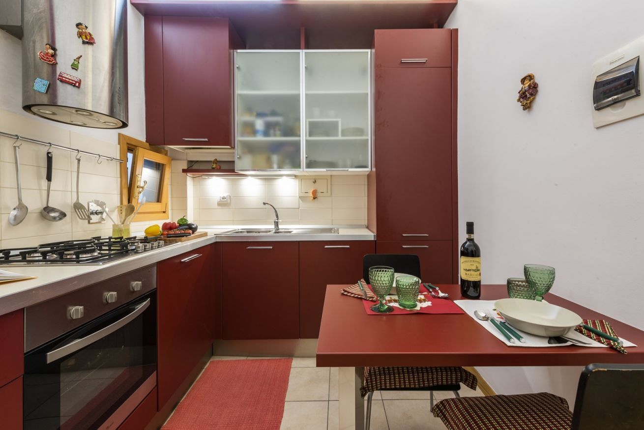 A compact kitchen with red cabinets, a gas stove, and a dining area with a table set for two.