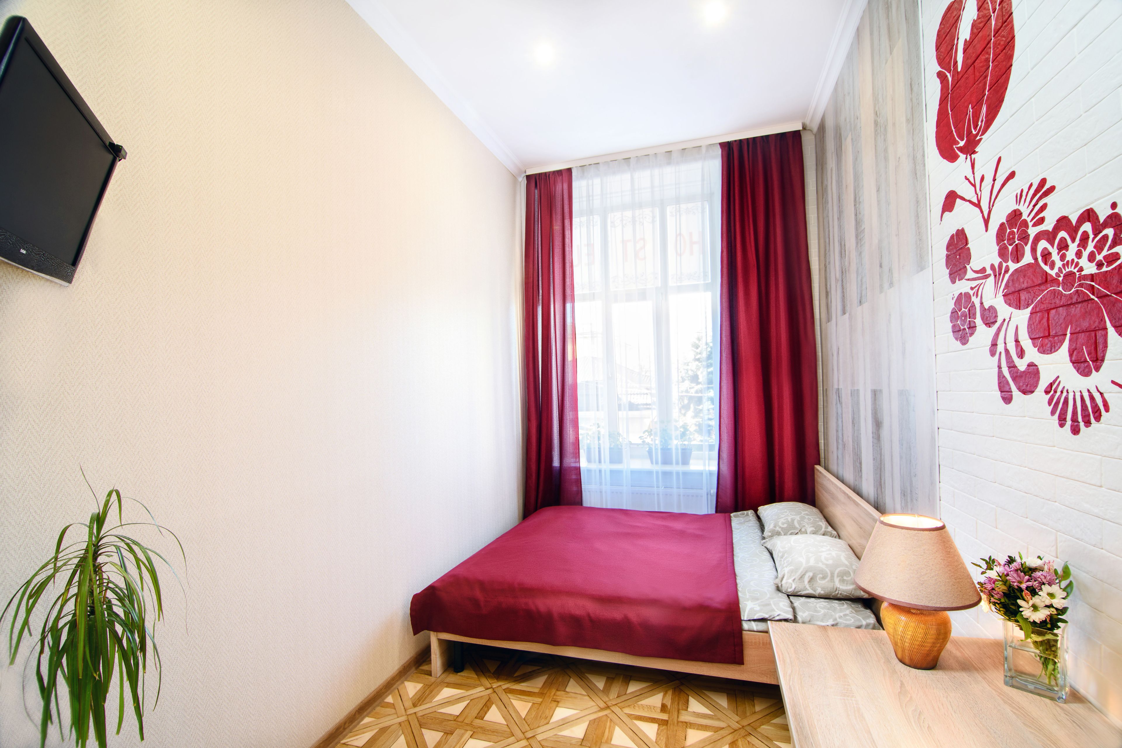 A bedroom with a bed, a bedside table with a lamp, a plant, and a wall-mounted TV.