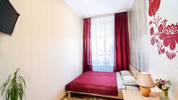 A bedroom with a bed, a bedside table with a lamp, a plant, and a wall-mounted TV.