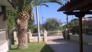 A courtyard with a palm tree, a stone wall, and a metal gate. - PEGGY'S VILLA 50 SQM (Κινέτα)