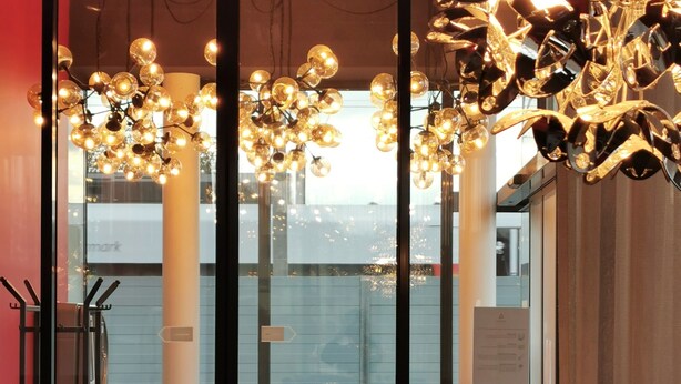 Un intérieur moderne agrémenté d’une sculpture métallique décorative placée sur un piédestal, de grandes fenêtres et de luminaires sphériques suspendus.