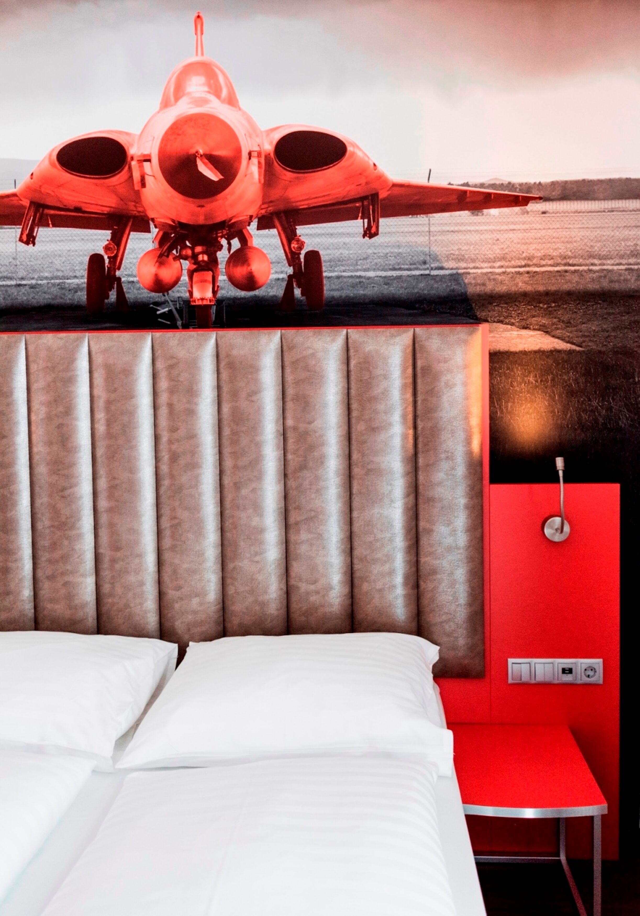 Une pièce avec un lit, un mur rouge et une fresque représentant un avion rouge.