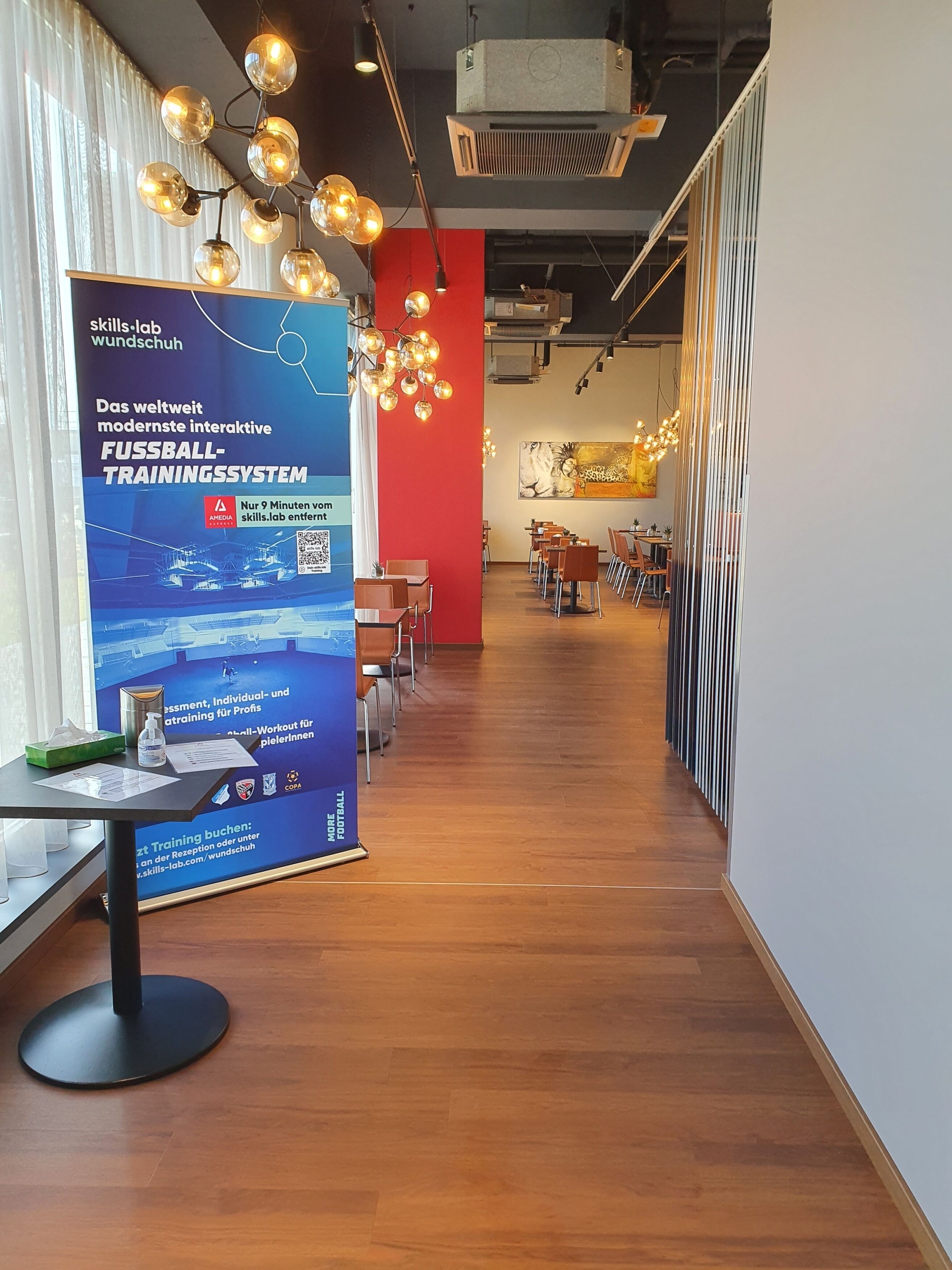 A modern indoor space with a wooden floor, a reception desk, and a large poster advertising a football training system.