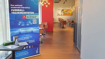 A modern indoor space with a wooden floor, a reception desk, and a large poster advertising a football training system.