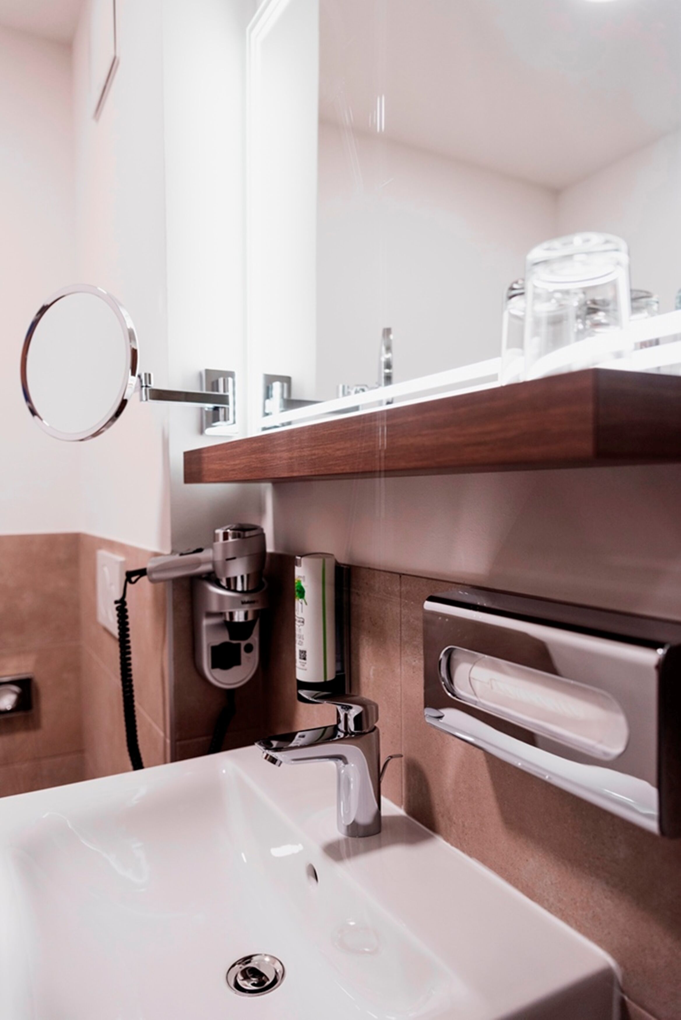 A modern bathroom with a white sink, a mirror, a hairdryer, and a towel rack.