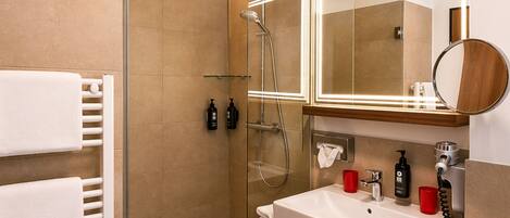 Un baño moderno con cabina de ducha de vidrio, lavabo blanco e iluminación integrada en un espejo.
