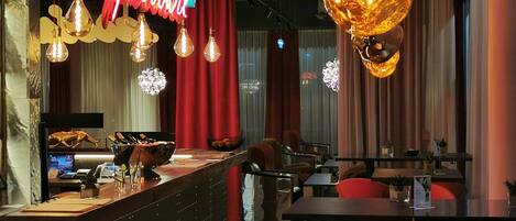 A modern bar area with a neon sign, hanging pendant lights, and a counter with a digital display.