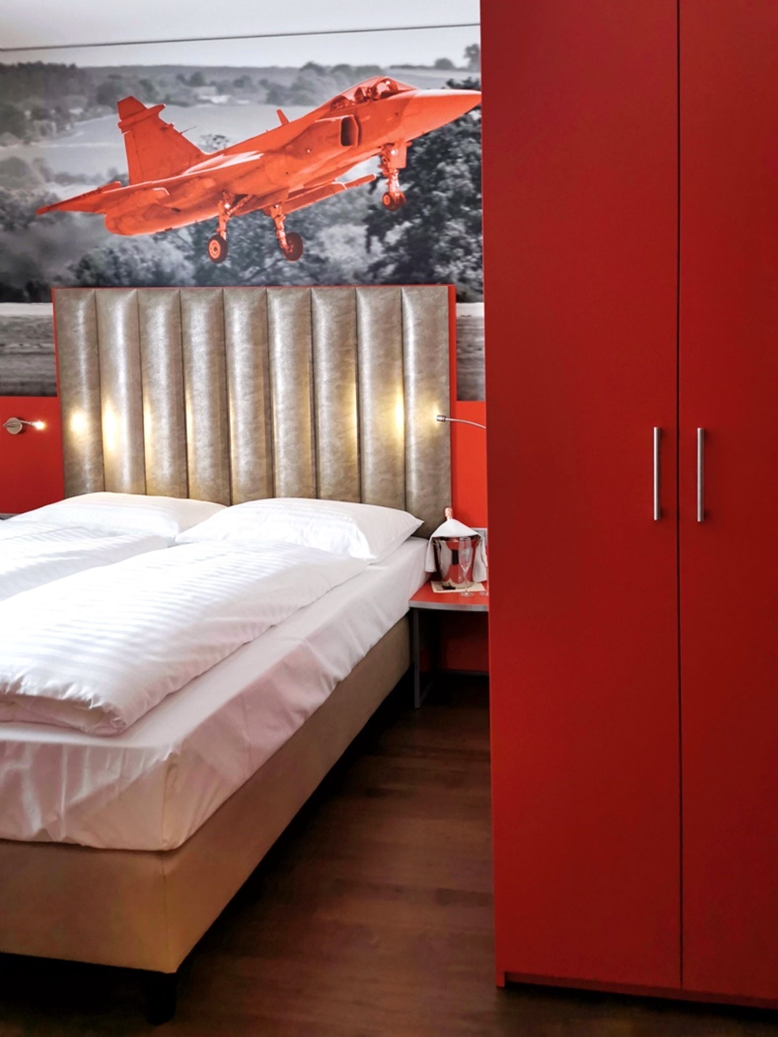 A bed with a headboard, a nightstand with a lamp, and a red wardrobe.