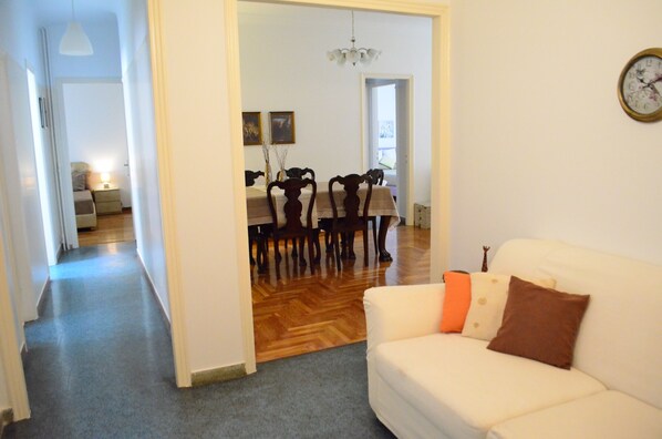 A living room with a white sofa, a dining table with chairs, and a chandelier. - PEDION AREOS PARK 5, sleep 8-12, 4-bedr, 2 bathrooms, Metro, Museum in 150m (Αθήνα)