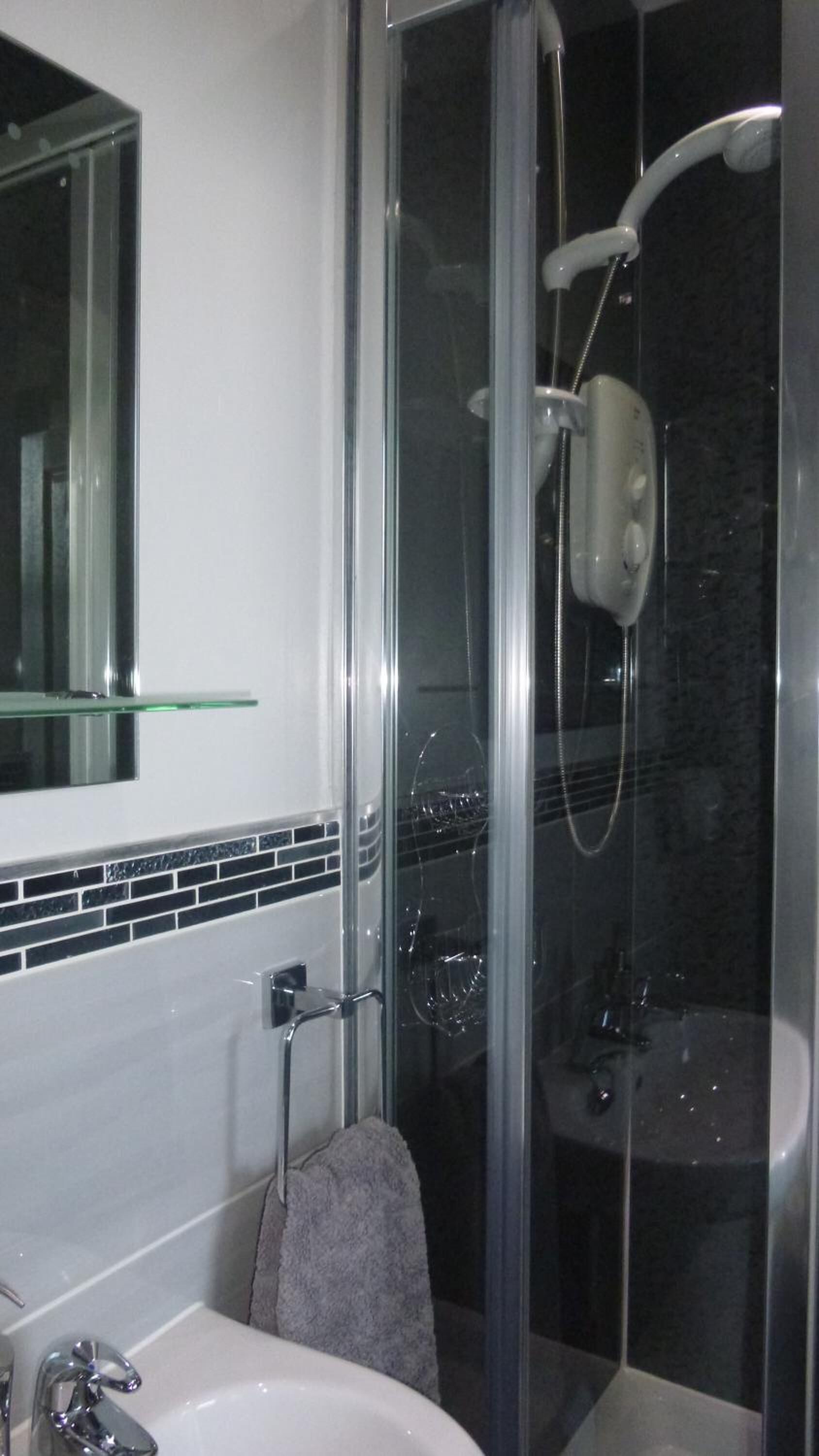 Un baño moderno con cabina de ducha de vidrio, estante de vidrio sobre el lavamanos y un perchero para toallas.