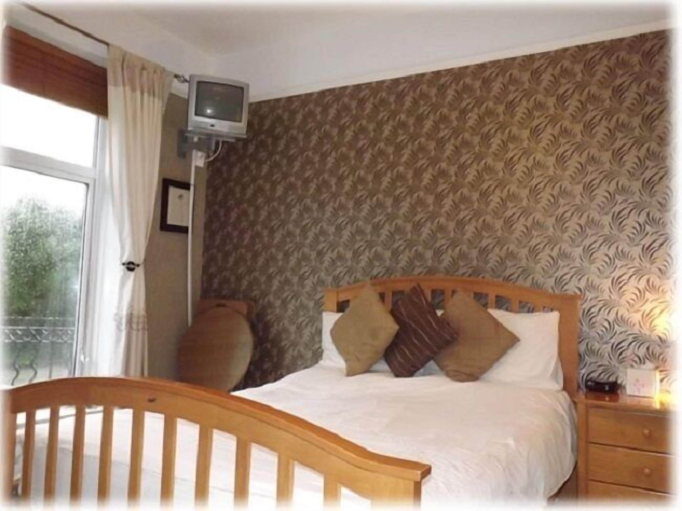 A bedroom with a wooden bed, a television on a stand, and patterned wallpaper.