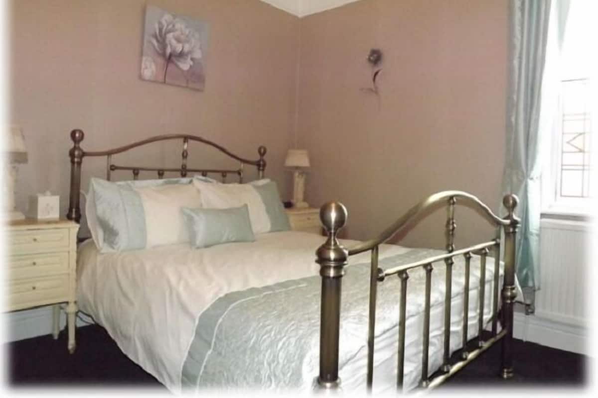A bedroom with a four-poster bed, a nightstand with a lamp, and a wall-mounted light fixture.