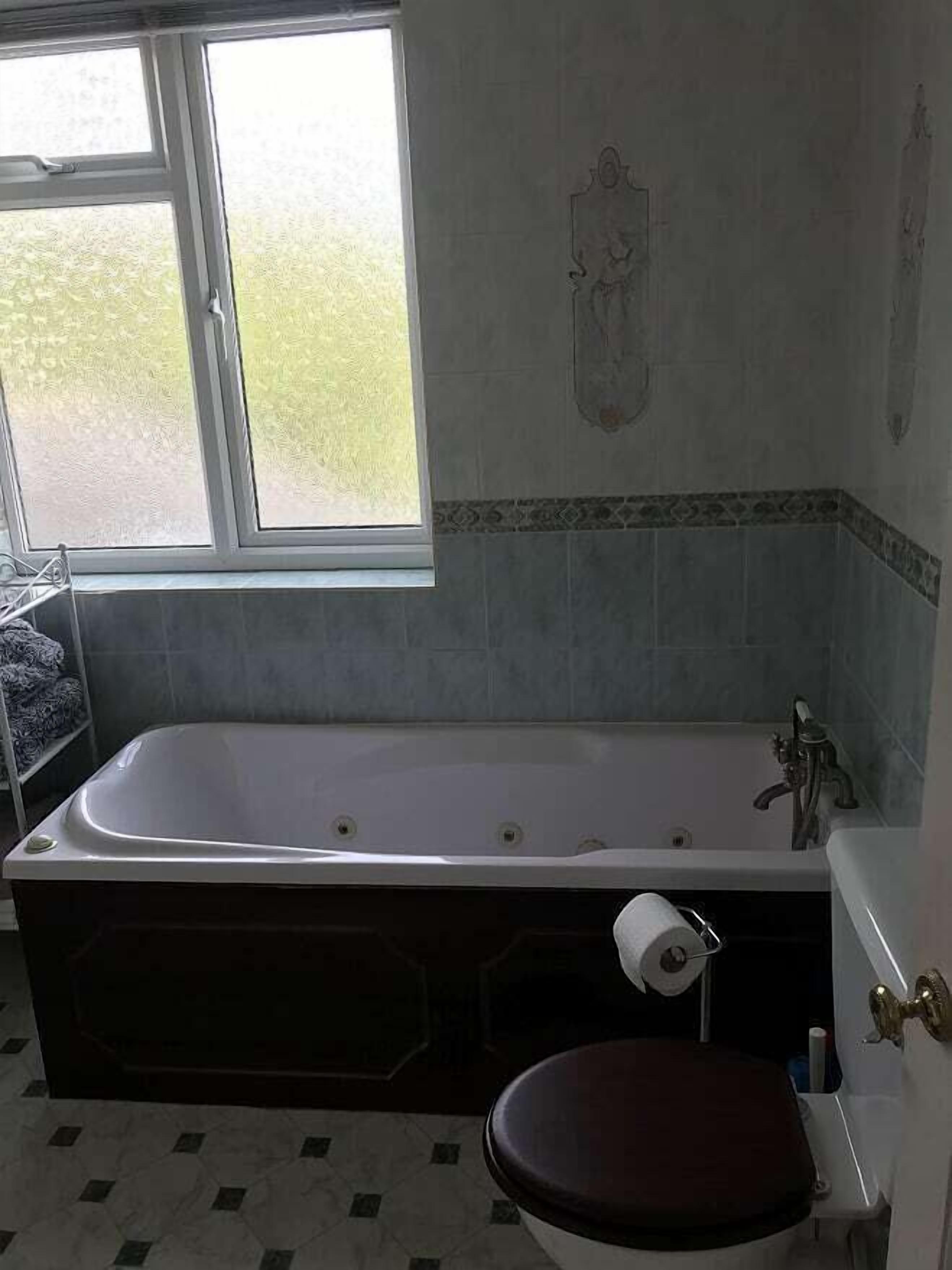 A bathroom with a bathtub, toilet, and a window.
