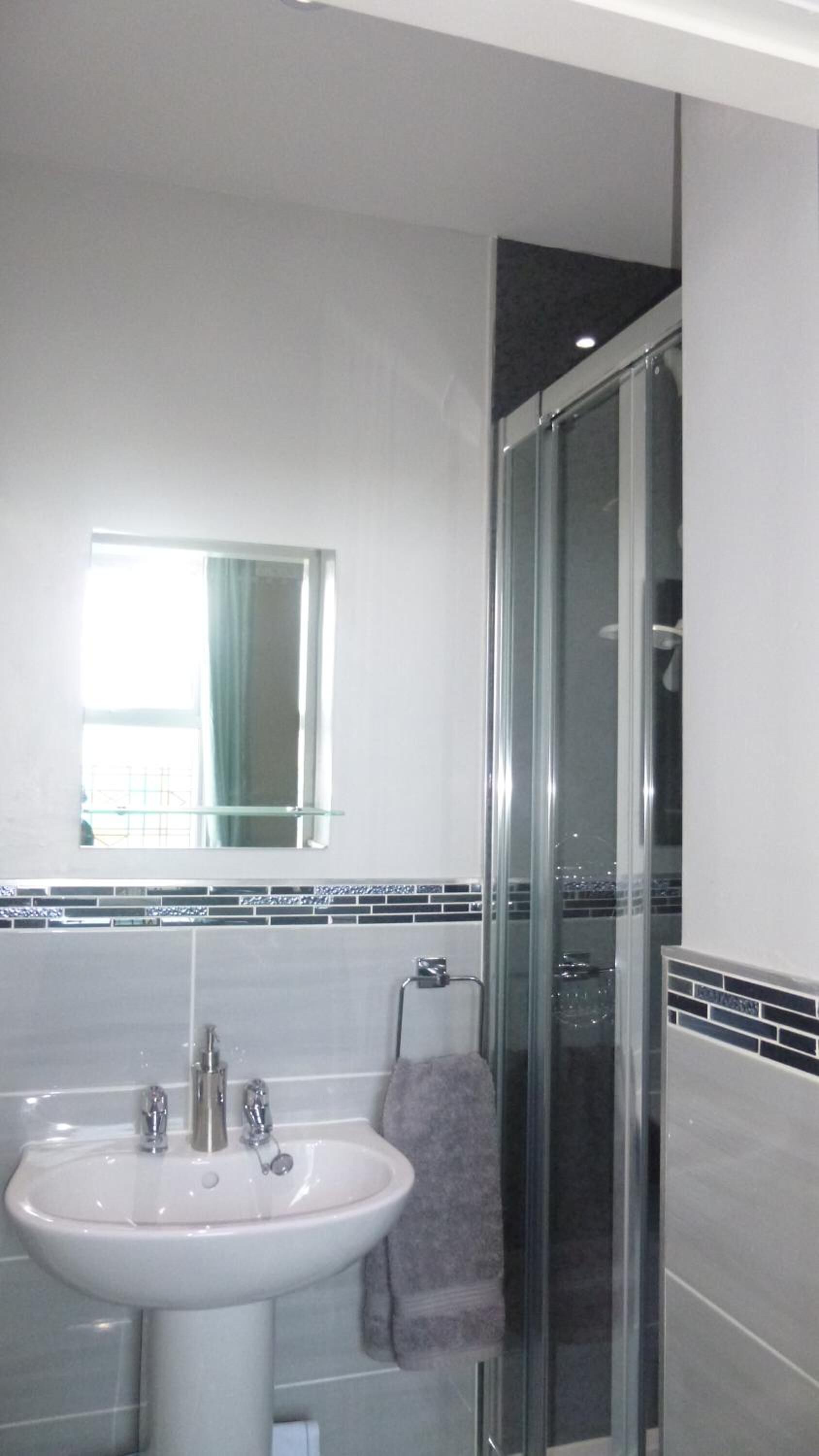 Une salle de bain moderne avec un lavabo blanc, un miroir et une cabine de douche en verre.