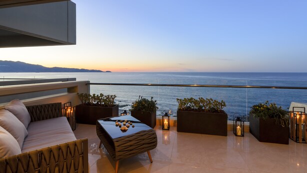 Un espace de détente extérieur moderne avec vue sur la mer, comprenant un canapé, une table et des plantes en pot.