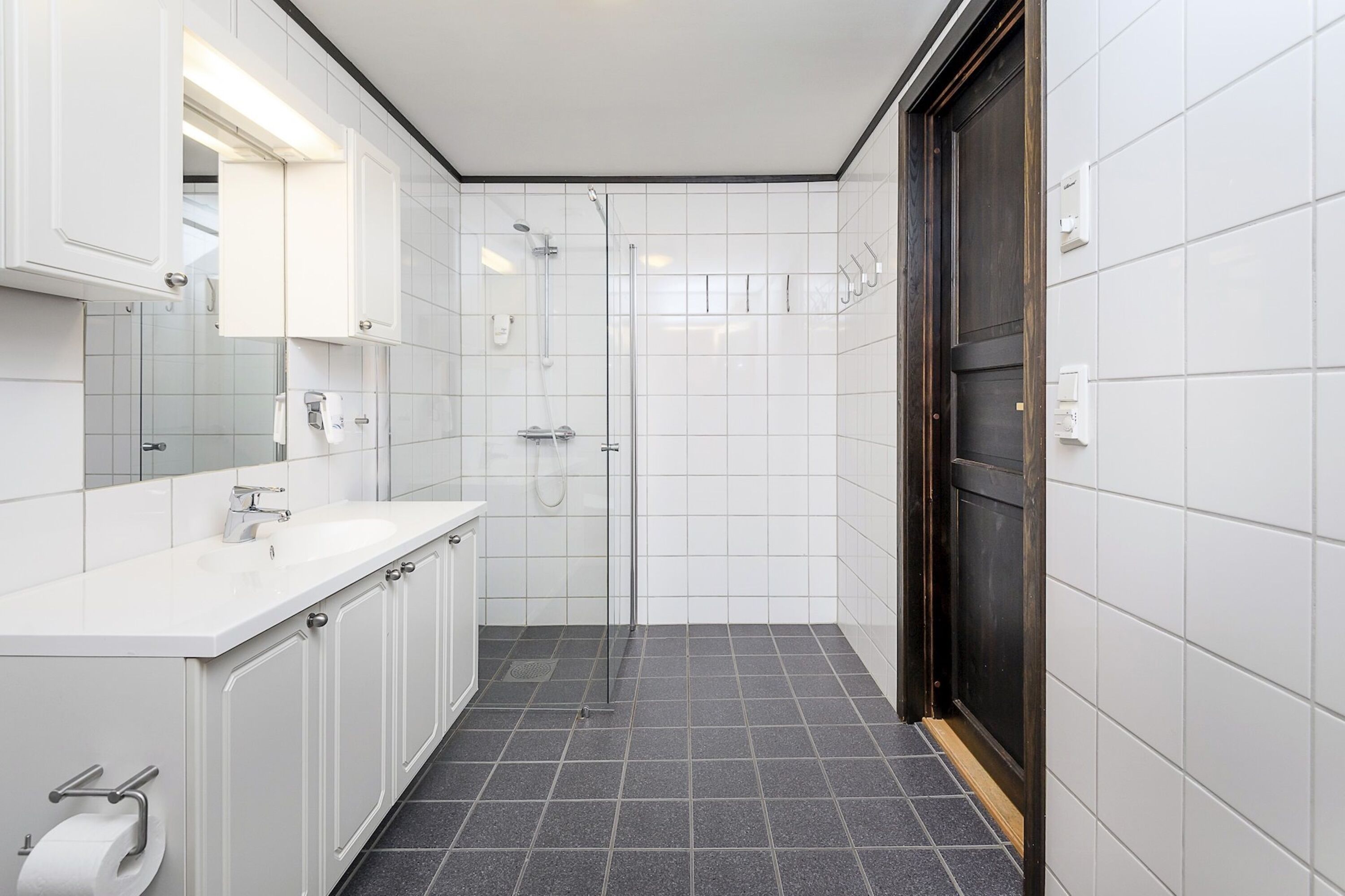 A modern bathroom with white tiles, a shower, a sink, and cabinets.