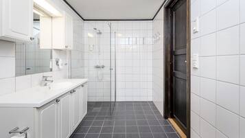 A modern bathroom with white tiles, a shower, a sink, and cabinets.