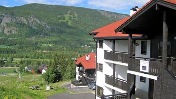 A two-story building with a red roof, wooden balconies, and a paved driveway.
