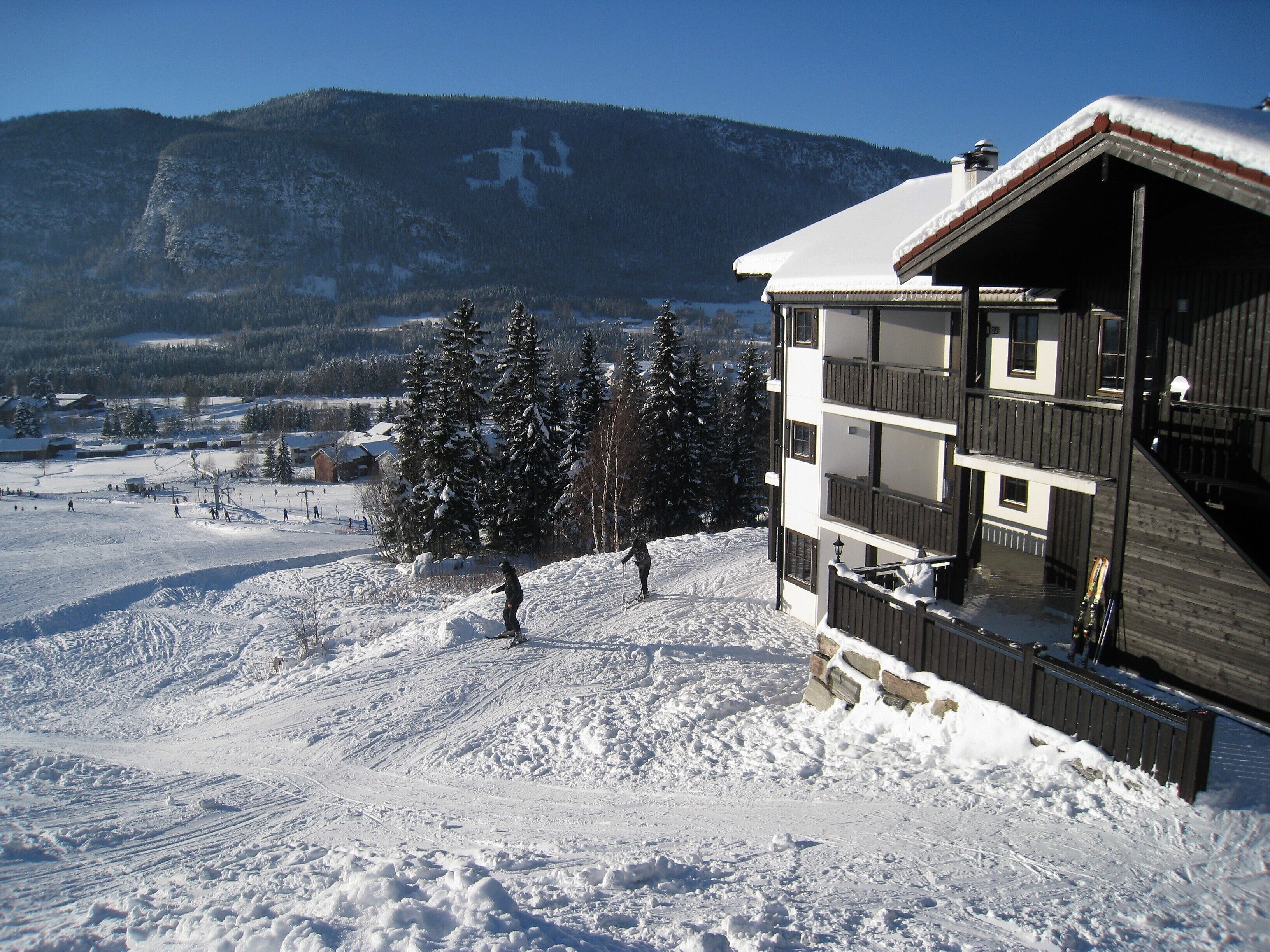 Une station de ski enneigée, avec un immeuble à plusieurs étages doté de balcons et une piste de ski en arrière-plan.