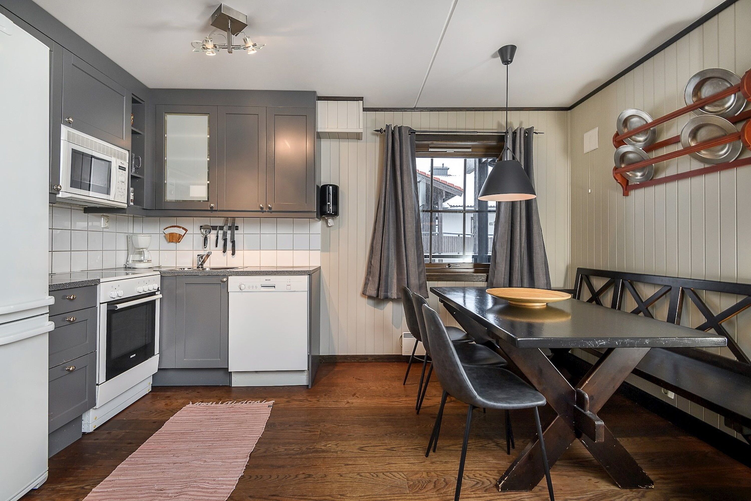 A modern kitchen with grey cabinets, a microwave, a dishwasher, and a dining area with a bench and table.
