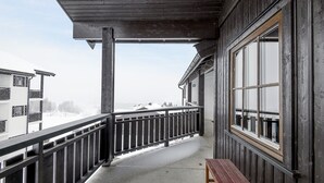 Un balcón con baranda de madera, una banca y vistas de edificios nevados.