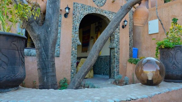 A stone archway leading to a building with a heart-shaped design, surrounded by potted plants and a spherical decorative object. - Gîte d'étape Imsker (Marrakech)