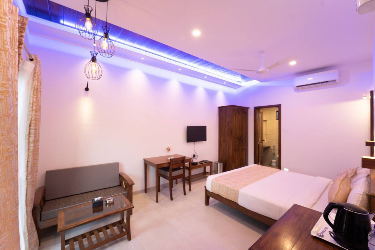 A hotel room with a bed, a desk with a chair, a sofa, a coffee table, and a TV mounted on the wall.