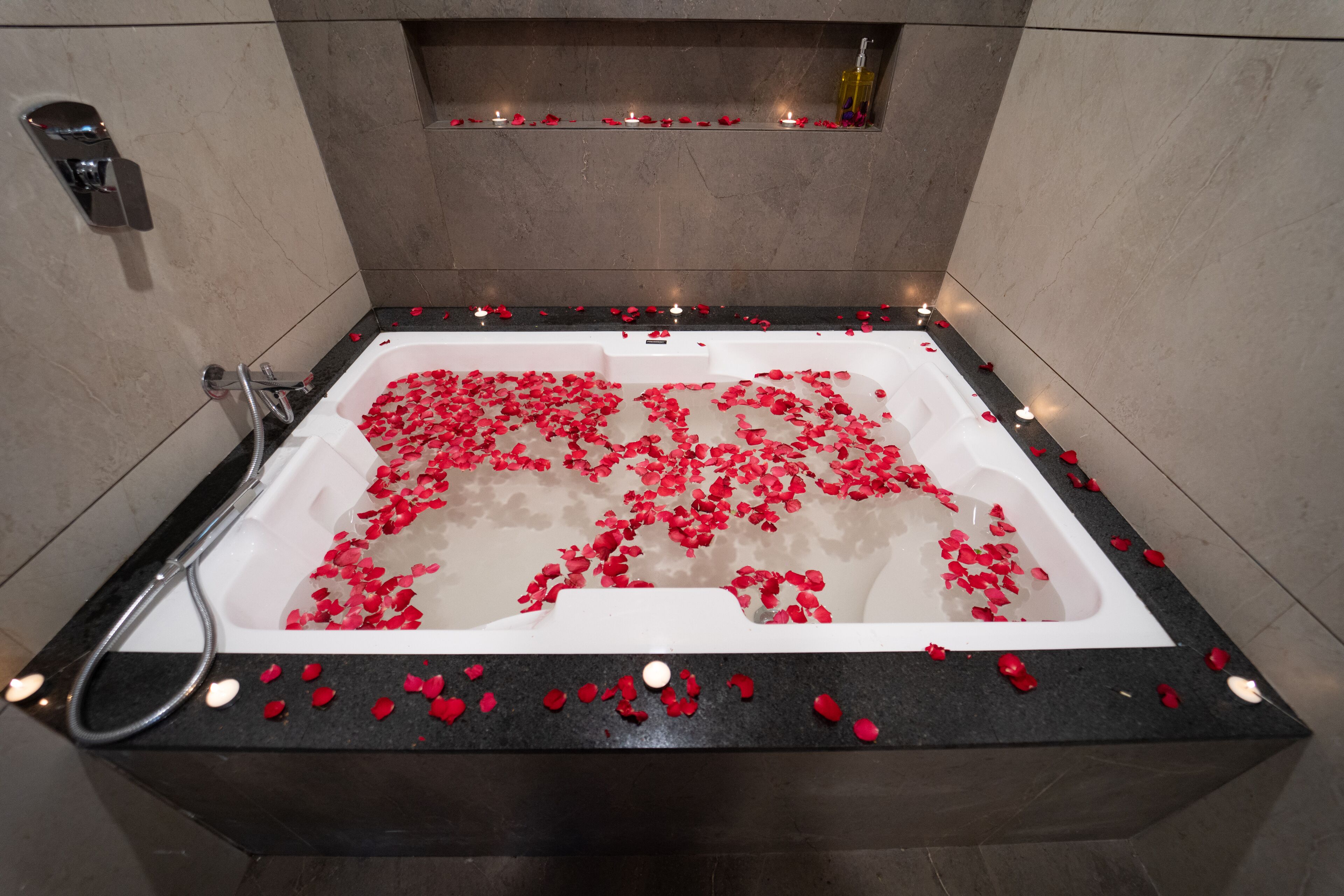 Un baño moderno con una bañera llena de pétalos de rosa y velas, una zona de ducha y un estante con velas.