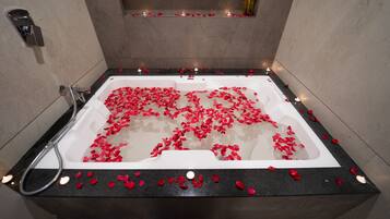 Un baño moderno con una bañera llena de pétalos de rosa y velas, una zona de ducha y un estante con velas.