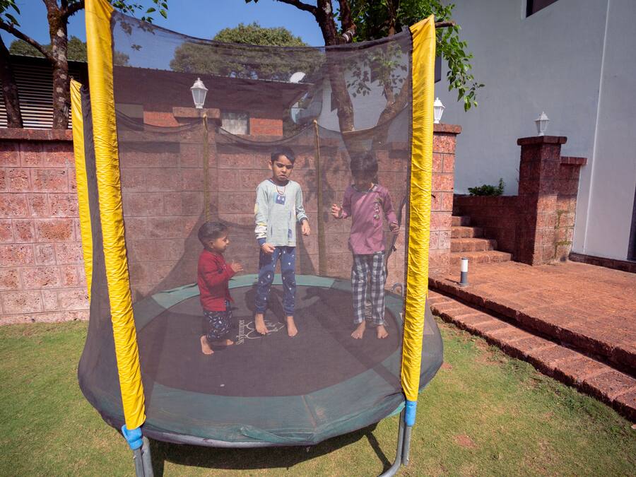 A trampoline with a safety net in a backyard with brick steps and a white building in the background.