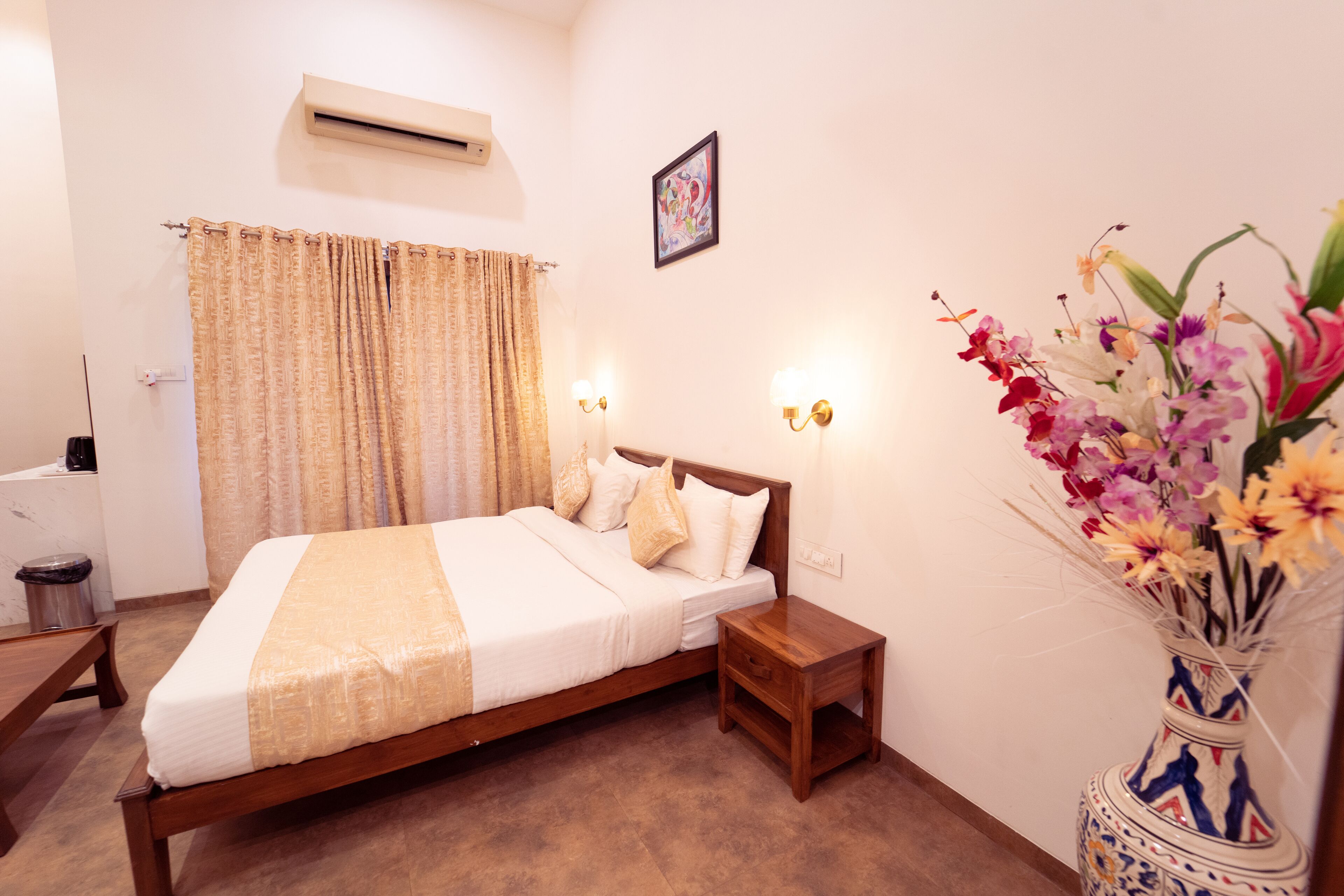 Un dormitorio ordenado con cama, mesitas de noche, un jarrón de flores y un aire acondicionado de pared.