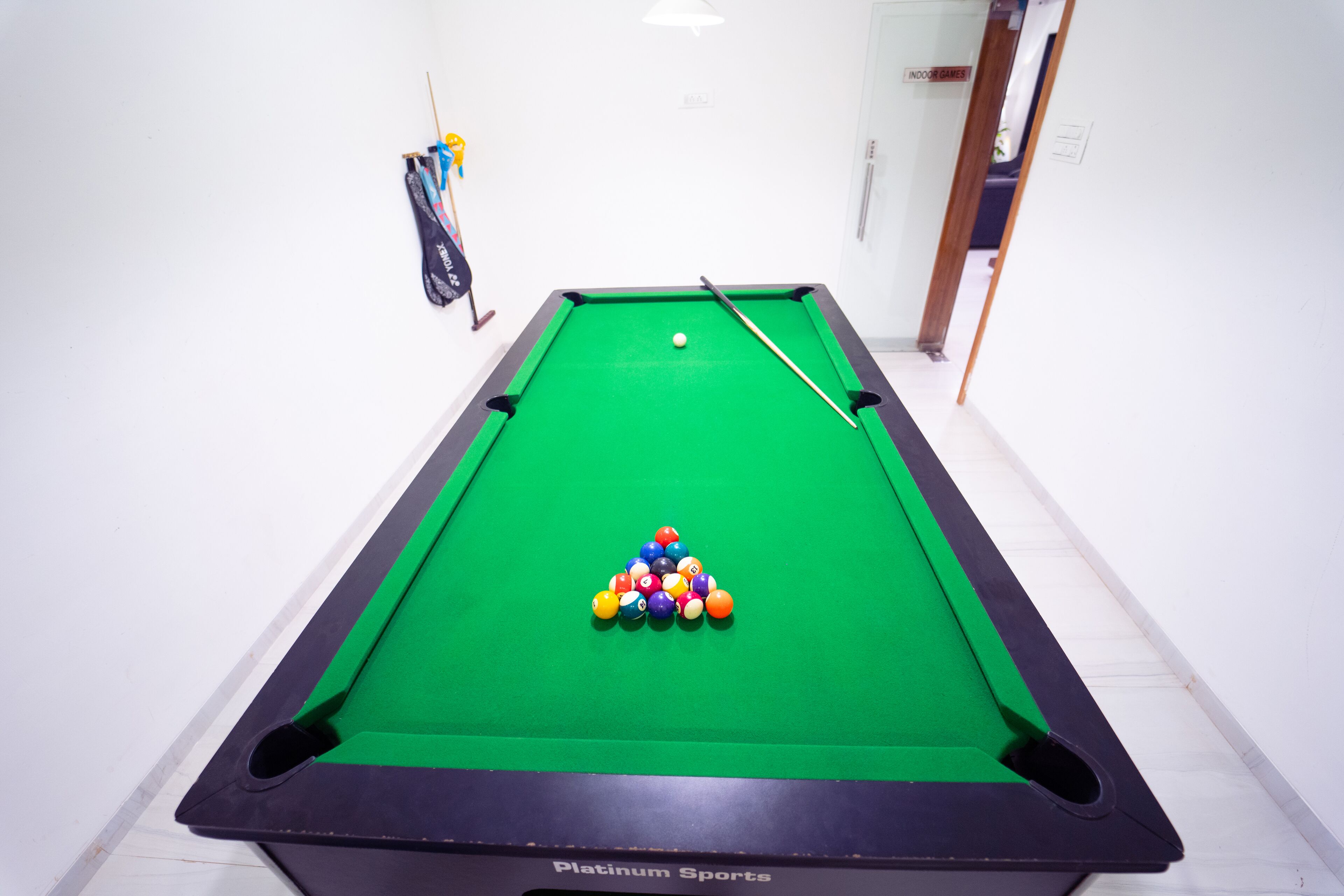 Una mesa de billar con un juego de bolas dispuestas en forma de triángulo, una cola de billar y un letrero que dice 'JUEGOS INTERIORES'.