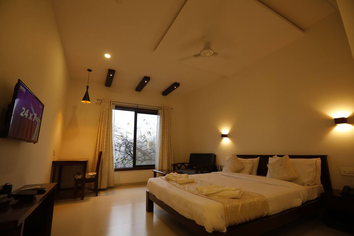 A bedroom with a large bed, a desk, a chair, a TV, and a window with curtains.