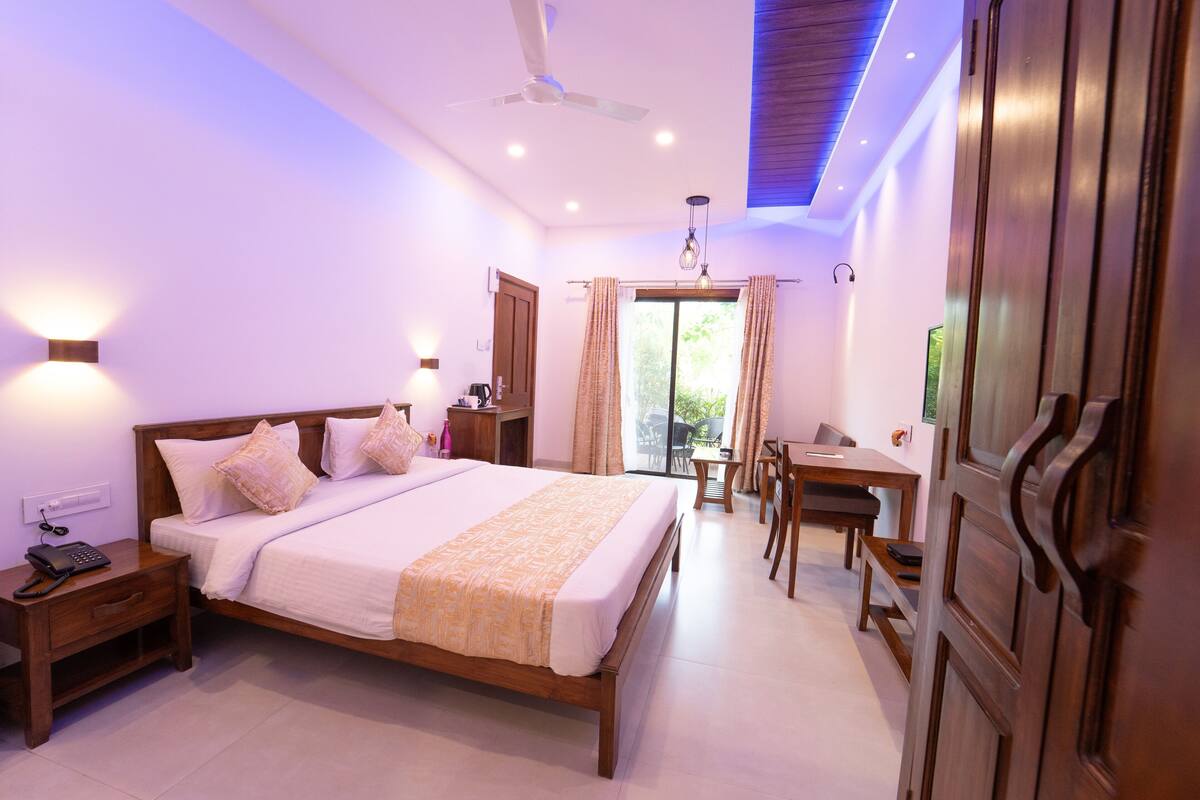 A hotel room with a bed, bedside table, lamp, and a view of the outdoors.