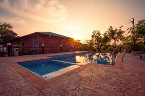 A rectangular swimming pool with a stone deck, surrounded by a brick building and trees. - La Serene Resort & Spa (Mahabaleshwar)