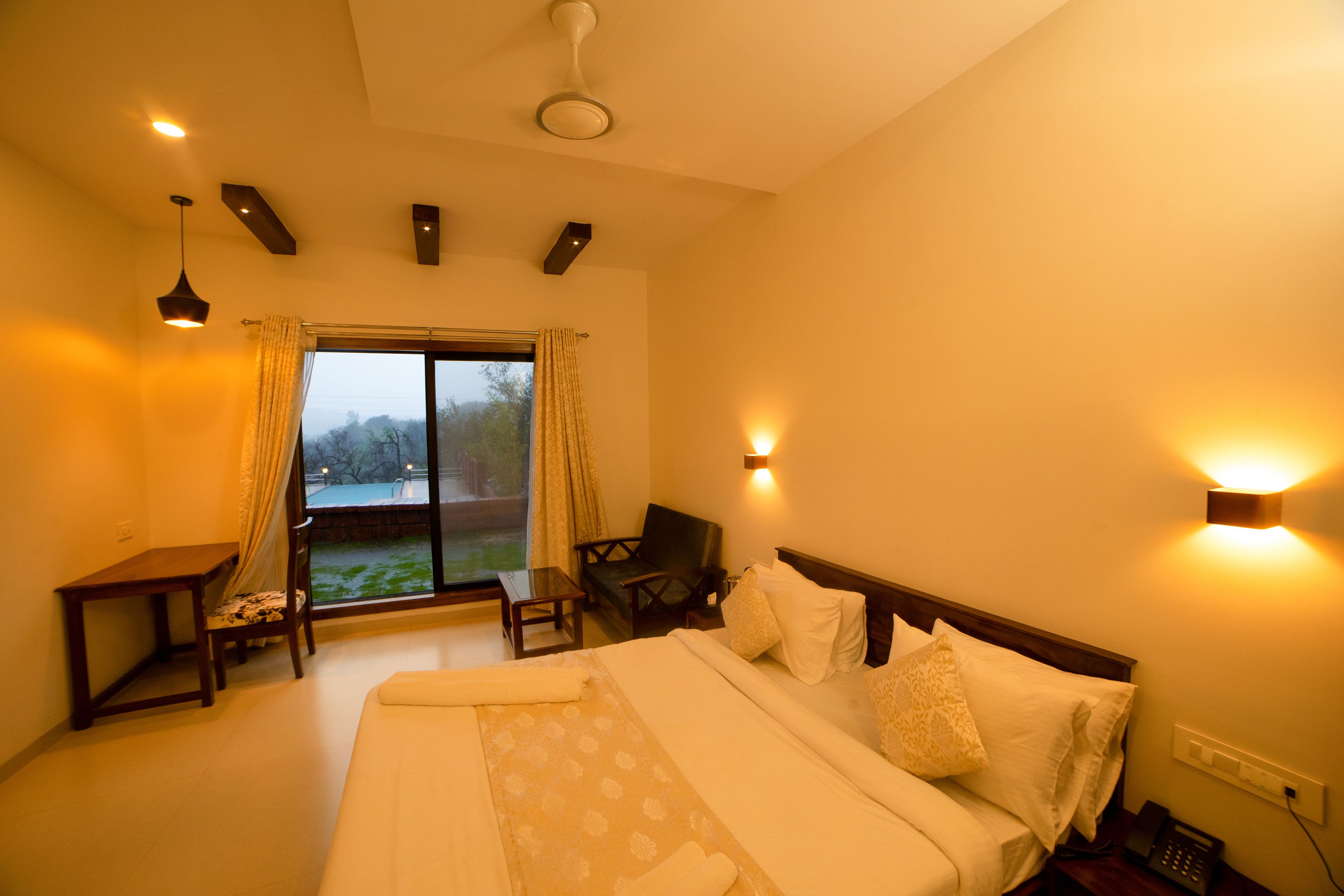 A hotel room with a large bed, a desk, a chair, and a view of the outdoors.