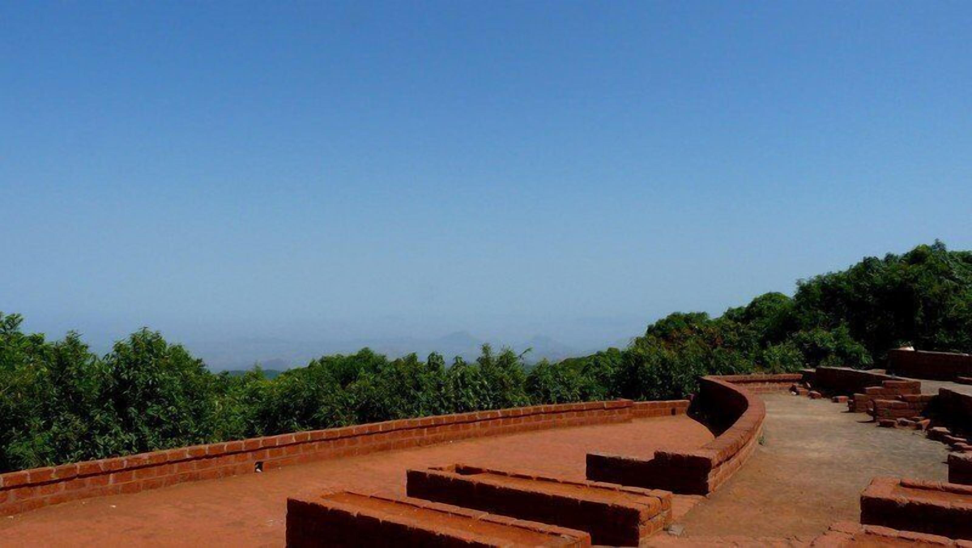 A terraced structure with steps leading up to a higher level, surrounded by greenery and a clear sky.