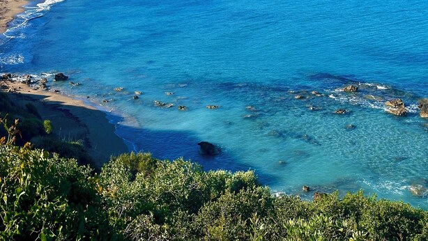 A coastal view with clear blue waters, a sandy beach, and lush greenery.