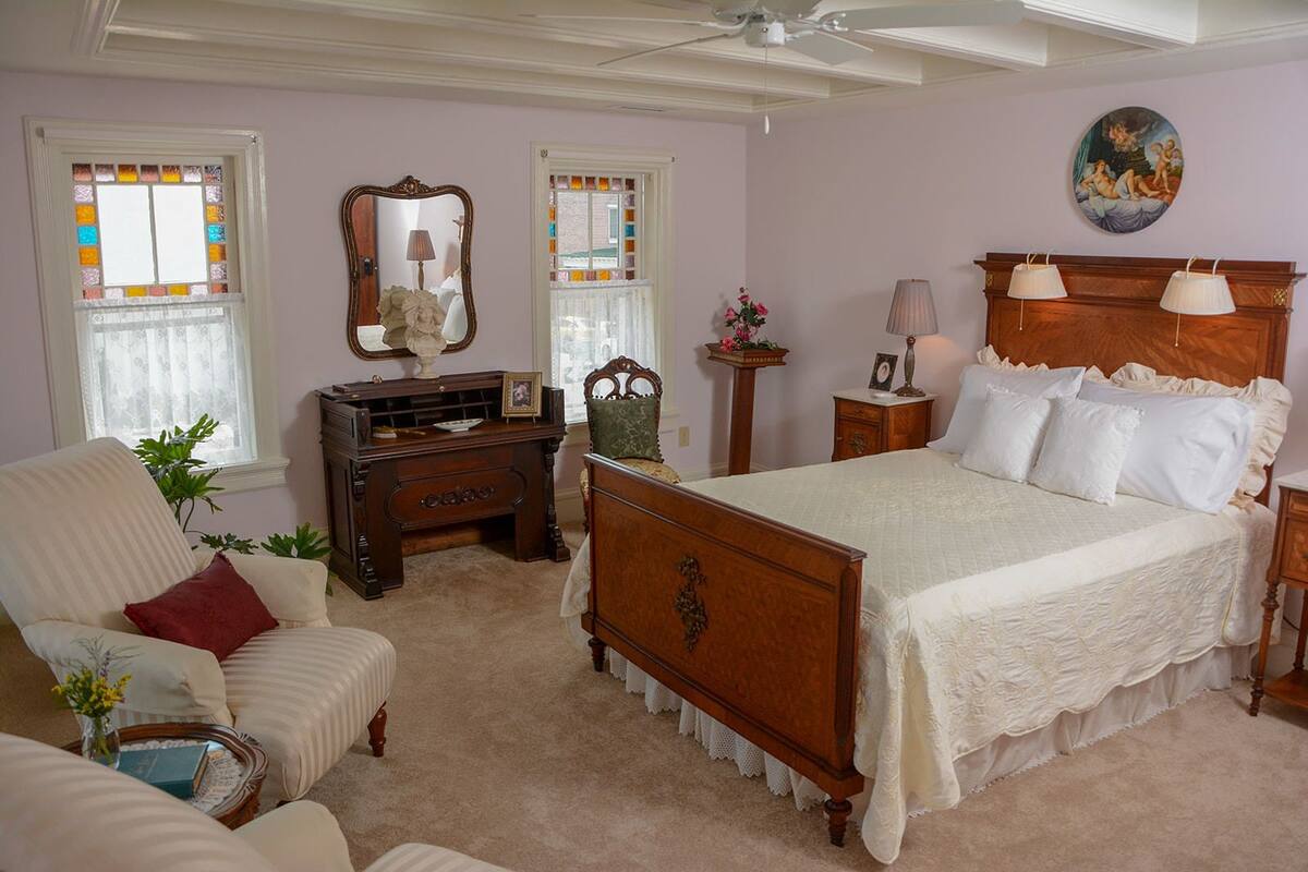 A bedroom with a large bed, a dresser, a chair, and a ceiling fan.