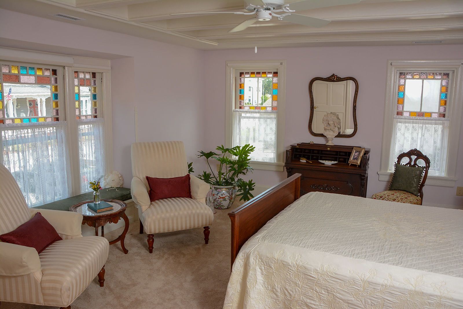Un dormitorio con una cama grande, dos sillones, una mesita, un aparador y un espejo.