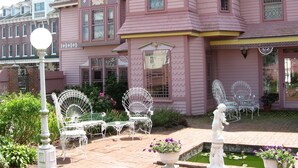 A pink Victorian-style house with a garden patio featuring white metal chairs and a small fountain. - The Towers Bed & Breakfast (Milford)