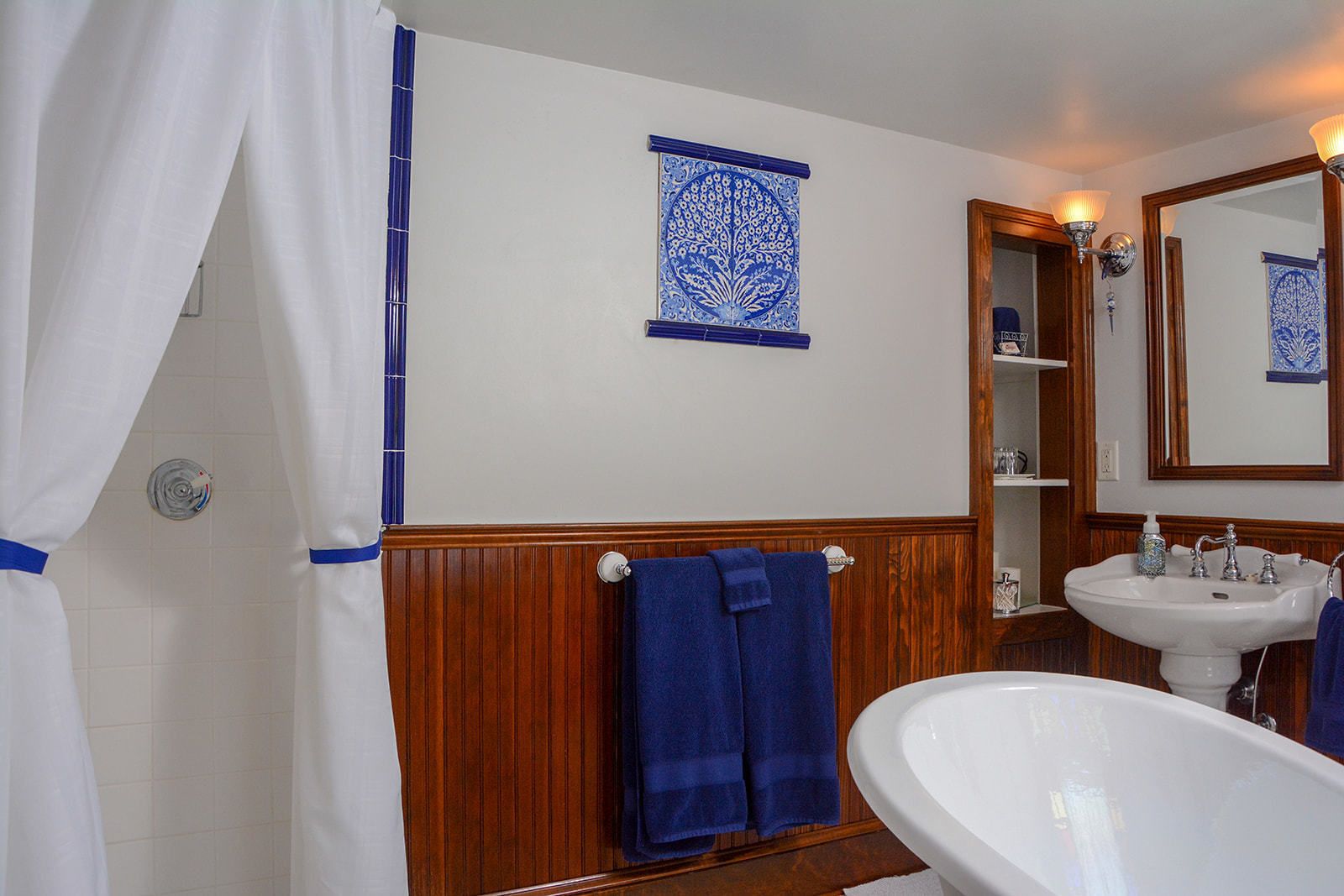 Un baño con paneles de madera, un lavamanos blanco, una toalla azul y baldosas azules con diseño en la pared.